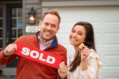 Couple holding the key and sold banner in front of their new home from Rolwes Company.
